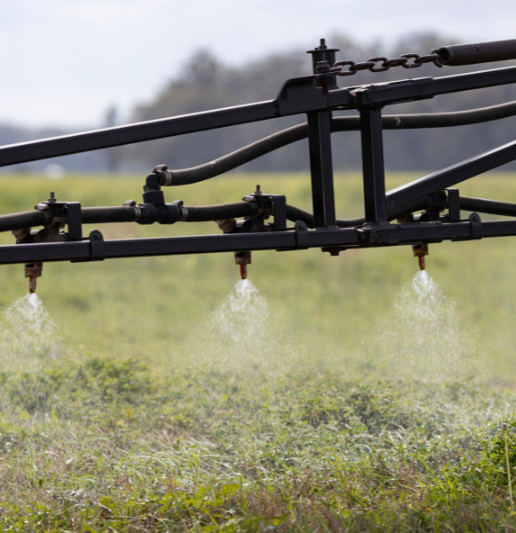 Close-up of an agricultural sprayer applying liquid over a green field.