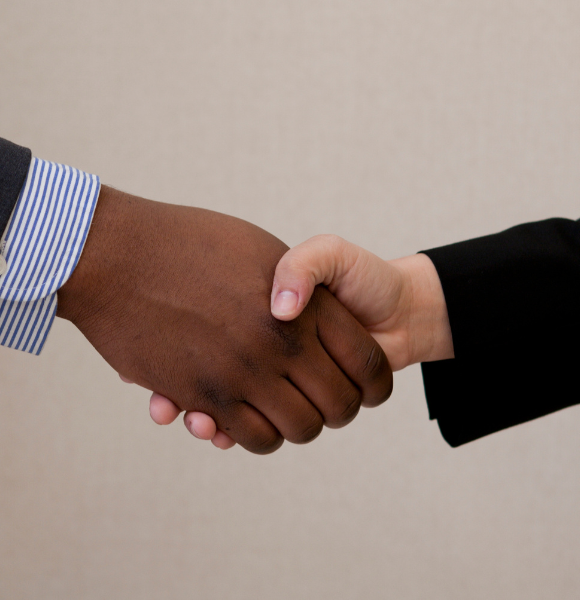 Close-up of two people shaking hands, one in a dark gray suit and the other in a black suit.